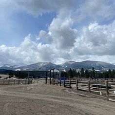 a dirt field with mountains in the background and a fenced off area to the side