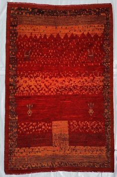 an old red rug is laying on a white sheet with some brown and orange designs