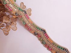 a decorative piece of art on a white surface with gold trimmings and colorful beads