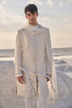 a man standing on top of a beach next to the ocean wearing a white outfit