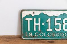 a green and white license plate on a wooden shelf with the number thirteen9 colorado