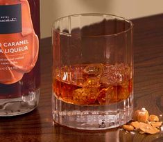 a bottle of liquor next to a glass filled with ice and nuts on a wooden table