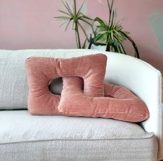 a pink corded pillow sitting on top of a white couch next to a potted plant