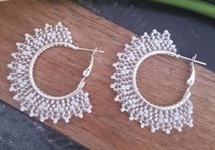 two pairs of white lace hoop earrings sitting on top of a wooden table next to a plant