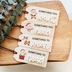 three tags with santa claus saying on them sitting on a wooden board next to eucalyptus leaves