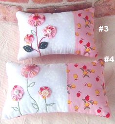 two pillows with flowers on them sitting next to each other in front of a brick wall