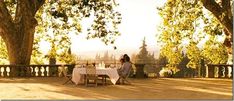 a woman sitting at a table in the shade of trees