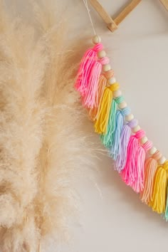 a rainbow tassel hanging on a wall next to a white chair with a wooden frame