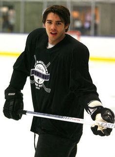 a man in black jersey holding a hockey stick and looking at the camera while standing on an ice rink