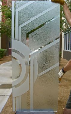 a man is working on a frosted glass door in front of a building with trees and bushes