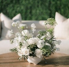 a vase filled with white flowers sitting on top of a wooden table next to pillows