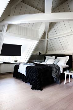 an attic bedroom with black and white bedding, wood flooring and slanted ceilings