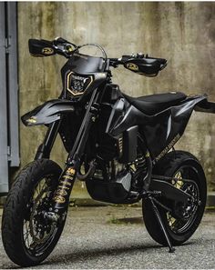 a black and gold motorcycle parked in front of a concrete wall with graffiti on it