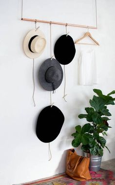 three hats are hanging on the wall next to a potted plant and a purse