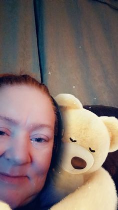 a woman with headphones on laying next to a teddy bear and smiling at the camera