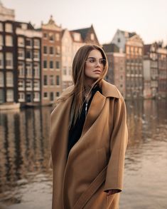 a woman is standing by the water wearing a coat