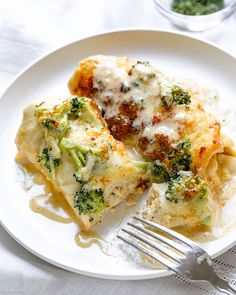 a white plate topped with lasagna covered in cheese and broccoli next to a fork