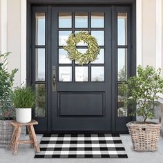 a black door with a wreath on it and two potted trees in front of it