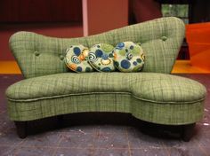 a green couch sitting on top of a tile floor next to a wall and window