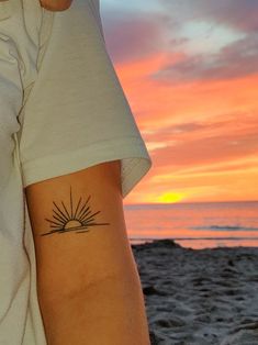 a person with a sun tattoo on their arm at the beach in front of an orange sunset