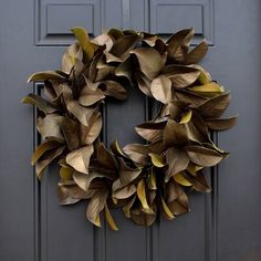 a wreath on the front door of a house that is painted gray and has yellow leaves