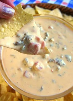 a hand holding a tortilla chip over a bowl of dip with chips on the side