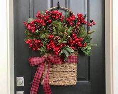 a basket filled with red berries and greenery hangs on the front door of a house