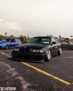 two cars parked in a parking lot next to each other with people looking at them