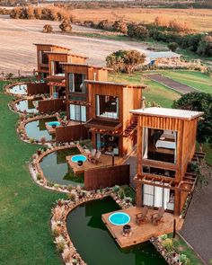 an aerial view of several wooden houses in the middle of a green field with water