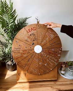 a wooden spinning wheel with writing on it sitting on a table next to potted plants