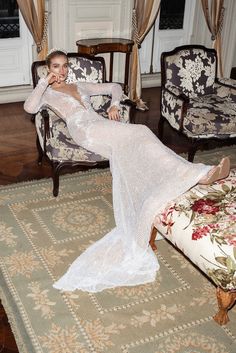 a woman in a white dress is sitting on a chair and posing for the camera