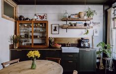 a kitchen with green cabinets and wooden table in the center, surrounded by potted plants