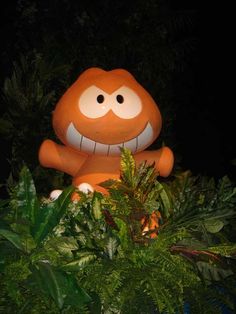 an orange monster sitting in the middle of some plants