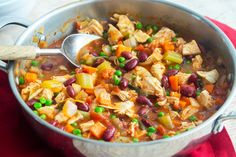 a pot filled with lots of food on top of a red cloth next to a wooden spoon