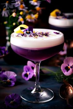 a purple drink in a wine glass with flowers around it