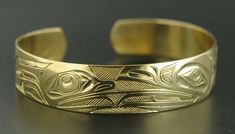 This is a new, hand-engraved, Northwest Coast Native First Nations gold cuff bracelet. Depicting Raven and Frog, this exquisitely carved gold bracelet measures 1/2" x 6" and will fit a wrist between 6 1/4" - 6 3/4" in circumference. It is signed on the inside by Kelvin Thompson and weighs roughly 18 grams solid 14k gold.Raven is often paired with Frog in Native art from the Pacific Northwest because Frog is viewed as the one who communicated Raven's knowledge to the people. These symbols also re Luxury Brass Bracelets With Polished Finish, Yellow Gold Cuff Jewelry For Anniversary, Carved Symbolic Yellow Gold Jewelry, Yellow Gold Symbolic Carved Jewelry, Adjustable Yellow Gold Hallmarked Cuff Bracelet, Formal Yellow Gold Brass Cuff Bracelet, Ceremonial Gold Bracelets With Polished Finish, Heirloom Yellow Gold Cuff Bracelet For Ceremonial Occasions, Ceremonial Heirloom Yellow Gold Cuff Bracelet