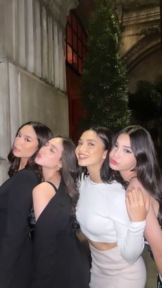 four beautiful women posing for the camera in front of a building at night with their arms around each other