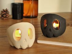 a skull lamp next to a book on a wooden table with two candles in the shape of skulls