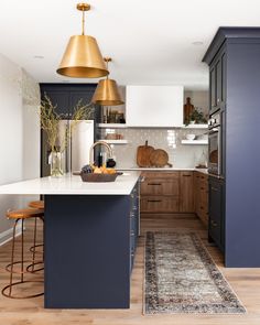 a kitchen with blue cabinets and gold pendant lights above the island countertop, along with an area rug on the hardwood floor