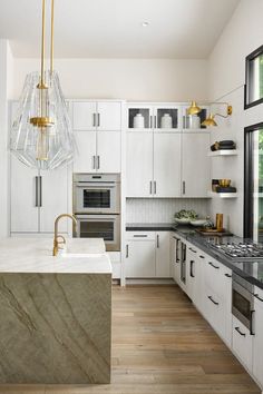 a kitchen with white cabinets and marble counter tops, gold accents on the faucet