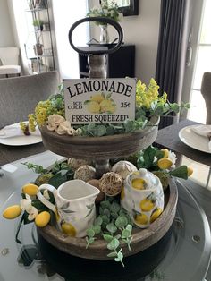 a tiered tray with lemons and flowers on top of a glass dining room table