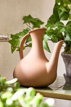 a brown vase sitting on top of a table next to a potted plant