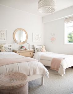 two twin beds in a white bedroom with pink and gray decor on the walls, along with a round mirror above them