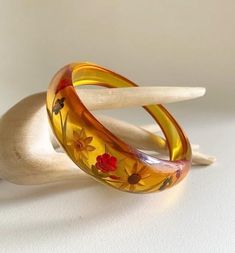 Gorgeous & becoming rare,  Art Deco 1930s reverse carved bakelite bangle In translucent, apple juice Bakelite which is asymmetrical in shape  Reverse carved to the thicker side with flowers & leaves design  looks lovely when it catches the light , almost glows , quite stunning ! Test Positive for Bakelite  bracelet size : Graduating from 1" (2.4 cm)  at widest part  down to 3/8" (0.8cm)  2 & 1/2 " (6.5cm)  internal diameter  In great vintage condition , very light surface wear commensurate  (very light scratches ) with its age , no cracks or damage & no wear to the reverse colours please note - any white marks in my photos are light reflection   A beatiful item for the collector ! Vintage Bakelite Bangle Jewelry, Vintage Bakelite Bangle, Vintage Amber Resin Jewelry, Vintage Amber Bangle Bracelet, Vintage Resin Bangle, Vintage Yellow Resin Jewelry, Vintage Lucite Bangle Bracelet, Vintage Resin Bracelet, Bakelite Bracelets