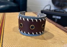 "One of a kind, upcycled leather bracelet made from used belts, upholstery scraps, and artistic findings. Every cuff is unique and made to wear and weather well.  Like high quality boots or your favorite leather journal, these cuffs get softer and more supple over time. The individual designs all start with the leather.  I use vintage belts, leather scraps, WW2 rifle holsters, and old horse bridles.  Each piece speaks to me, and informs the direction for the finished piece.  Adornments include found objects, printed leather, metal studs, gemstones, buttons - anything that will bring the cuff to life and make it a statement piece unlike any other. I prefer using a button & elastic closure when possible, as it makes the cuff fully adjustable.  It's a more labor and cost intensive process, bu Handmade Bohemian Leather Bracelet For Everyday, Bohemian Handmade Leather Bracelet For Everyday Use, Bohemian Handmade Leather Bracelet, Handmade Distressed Brown Leather Bracelets, Handmade Artisan Leather Bracelet, Adjustable Leather Cuff Bracelet, Adjustable Unique Leather Bracelet, Casual Leather Bracelet For Festivals, Rustic Leather Bracelet For Festivals