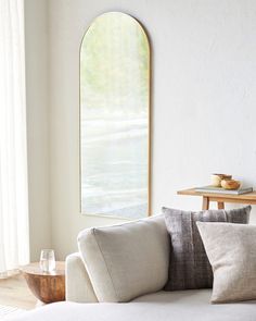 a living room with a white couch and round mirror on the wall next to it