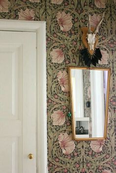 a mirror hanging on the wall in front of a door with pink flowers and leaves