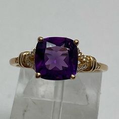 Set Securely In The Center Of This Ring Is A Cushion Cut Natural Amethyst Gemstone. The Amethyst Measures 8mm And Is Set With Four Prongs. It Has A Vibrant Deep Purple Color (Likely Heat Treated). The Amethyst Sits Just 1/4" Off Of Your Finger In A Decorative Cut Out Basket. The Band Has Small Diamonds Set Down Both Sides In A V Shape. It Is Currently A Finger Size 7 But The High Polished Shank Would Be Easy To Size Up Or Down (Locally). The Setting Is Solid Yellow Gold And Is Stamped 10k On The Elegant Purple Gemstones With Accents, Elegant Purple Gemstones With Diamond Accents, Fine Jewelry Purple Rings With Diamond Accents, Fine Jewelry With Purple Accent Stones, Purple Amethyst Gemstone With Center Stone, Fine Purple Jewelry With Accent Stones, Purple Fine Jewelry With Accent Stones, Classic Amethyst Rings With Gemstone Accents, Classic Purple Amethyst Ring With Vs Clarity