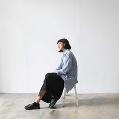 a woman sitting on a chair in front of a white wall and looking off to the side