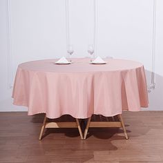 two empty wine glasses sit on top of a round pink tablecloth with wooden legs